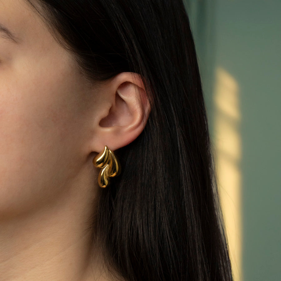 Damesmodel draagt gouden oorstekers met drie druppels, elegant en verfijnd